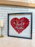 Black frame wedding flower frame with a heart of red paper roses, styled on a kitchen counter