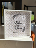 Full frame of white paper roses with a black arch welcome sign and names on the glass