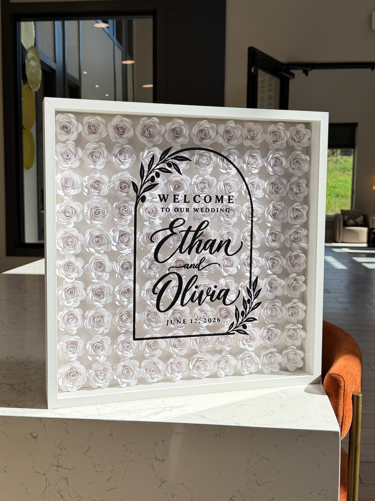 Full frame of white paper roses with a black arch welcome sign and names on the glass